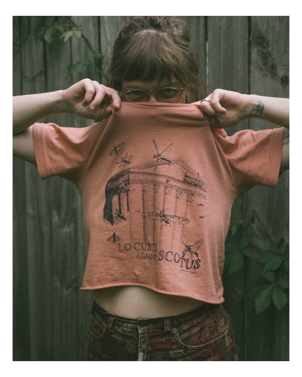 A woman wearing a cropped version of a screen printed t shirt with locusts flying around the supreme court of the United States