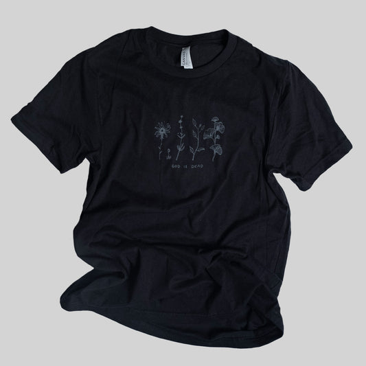 Black T shirt with a screen printed illustration of flowers and the handwritten text God Is Dead underneath. Soft style shirt
