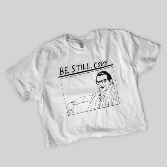 white cropped t shirt with an illustration of jeff goldblum in wes anderson's film the life aquatic. the text be still cody is above the drawing. the shirt is in the style of the sonic youth album goo