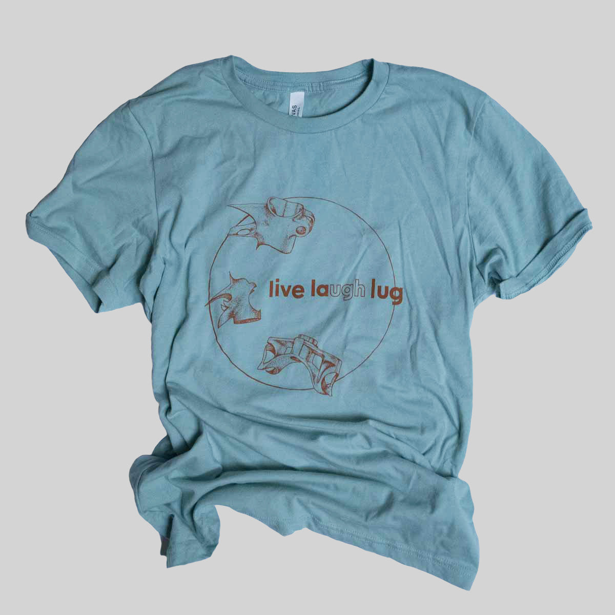Blue green t shirt with a screen printed line art illustration of three bicycle lugs in a circle with the text Live Laugh Lug. Ugh is highlighted. Ink is an earth tone red orange 